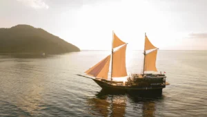 Beautiful traditional boat with open sails cruising through the calm waters of Komodo National Park on a full day tour