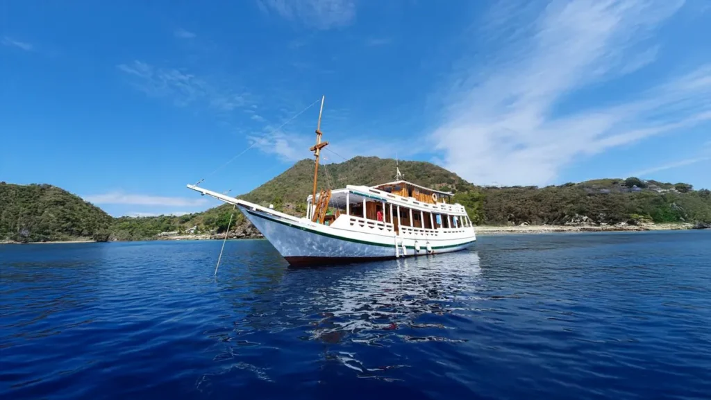 North Blue Phinisi anchored in clear Komodo waters with an island behind it