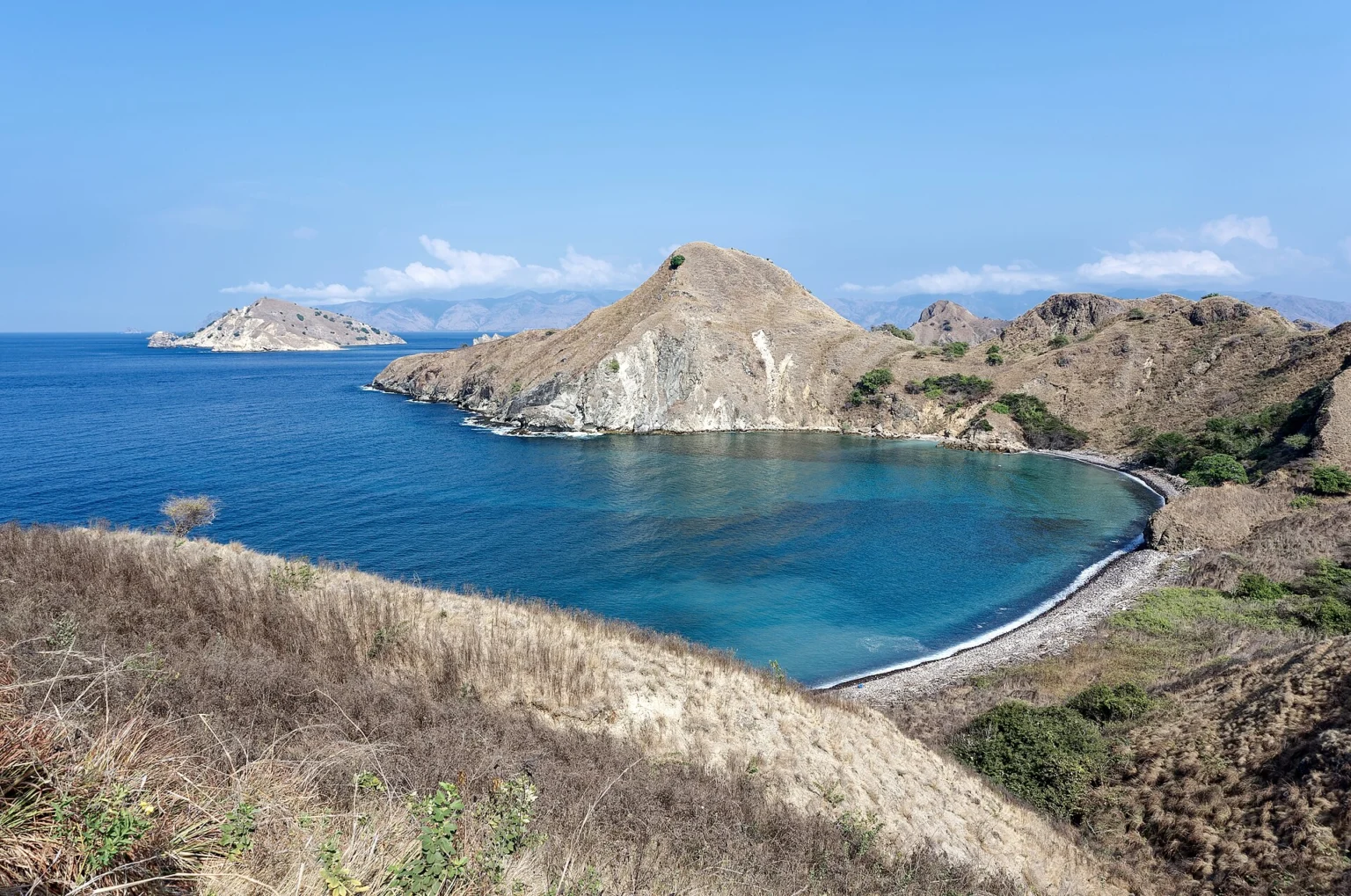 Padar Island dry hills and coastal bays — padar island sunrise trek Dry grassy slopes descend toward blue bays on Padar Island.